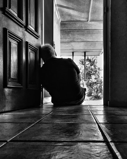 Black and white picture of Peter sitting on the floor, leaning against the door, facing the front porch with his back to the camera