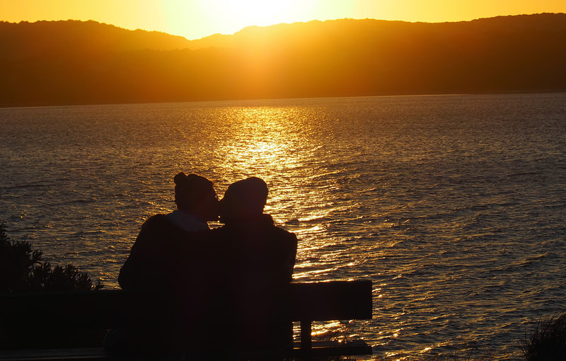 Daniel and his partner kissing as the sun sets in the sea