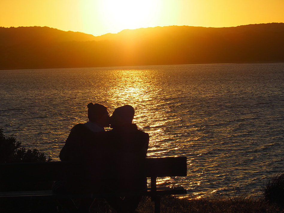 Daniel and his partner kissing as the sun sets in the sea